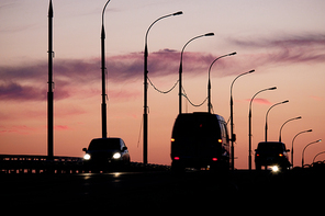 Silhouettes of cars and vans in front of pink-orange sunset sky with silhouettes of streetlamps