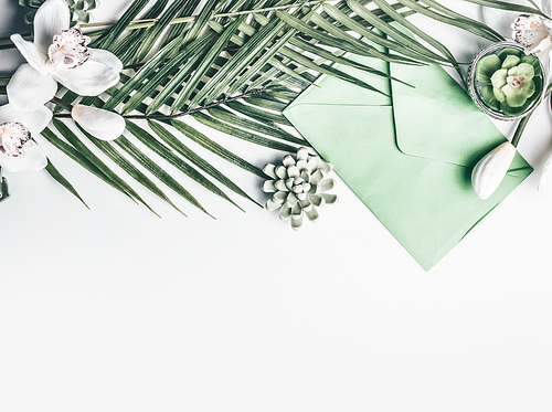 Green Tropical leaves with orchid flowers, envelope, and succulent decoration on white desktop background, top view, border