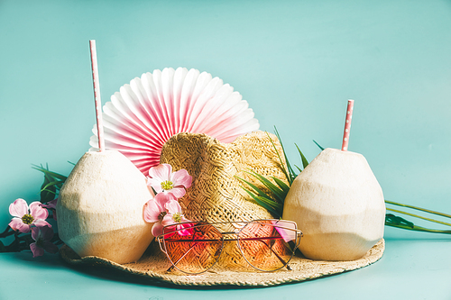 Summer holiday .  Beach accessories : straw hat, palm leaves, pink sun glasses, flowers and coconut cocktails on blue turquoise background, front view. Tropical vacation travel concept