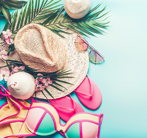 Summer holiday concept. Beach accessories : straw hat, palm leaves, sun glasses, pink  flip flops , bikini and coconut cocktail on blue turquoise background, top view. Tropical vacation travel concept