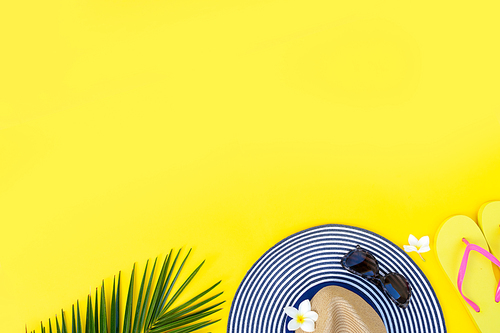 Summer flat lay scenery on yellow background with palm leaf , hat and flip flops, copy space
