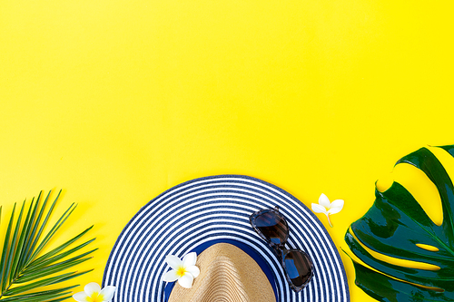 Summer flat lay scenery with hat and green leaves on bright yellow background with copy space
