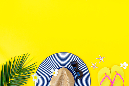 Summer flat lay scenery border on yellow background with palm leaf , hat and flip flops, copy space