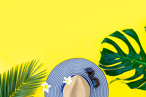 Summer flat lay scenery with hat and green leaves on bright yellow background, top view border with copy space