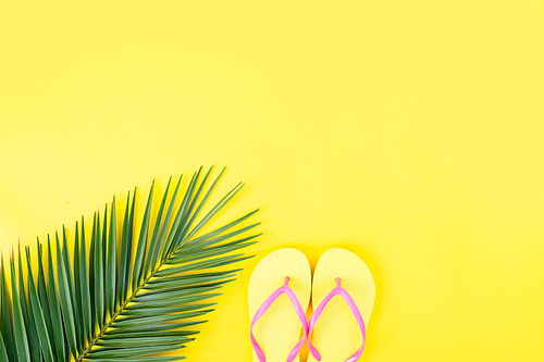 Summer flat lay scenery on yellow background with palm leaf and flip flops sandals, copy space