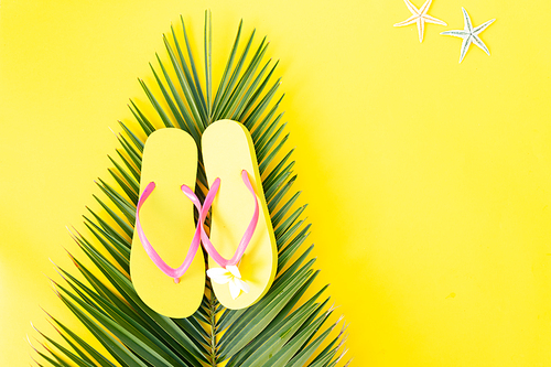 Summer flat lay top view scenery on yellow background with palm leaf and flip flops, copy space