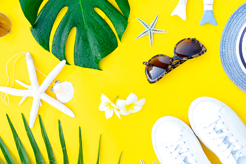 Summer flat lay with green leaves and shoes over yellow background