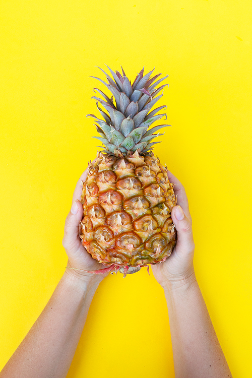 someones hands holding raw pineapple on yellow background
