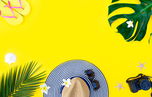 Summer flat lay scenery with hat and green leaves on bright yellow background, top view frme with copy space