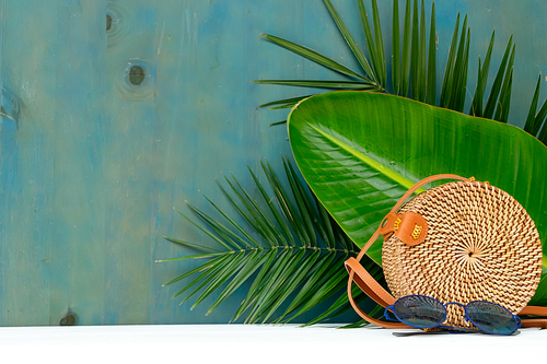Summer scenery with straw bag and tropical leaves, copy space on backdrop