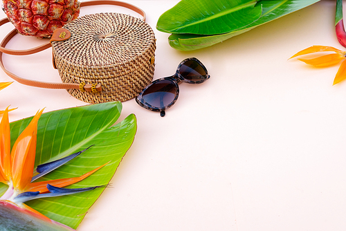 Summer flat lay scenery with tropical leaves, bag glasses on pink background with copy space