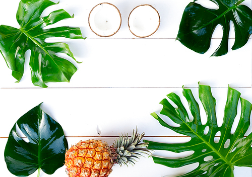 Summer flat lay scene with tropical leaves and pineapples frame on white wooden planks background with copy space