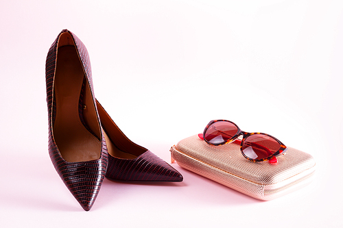 Pair of elegant leather high heel shoes with bag and sunglasses on pink background