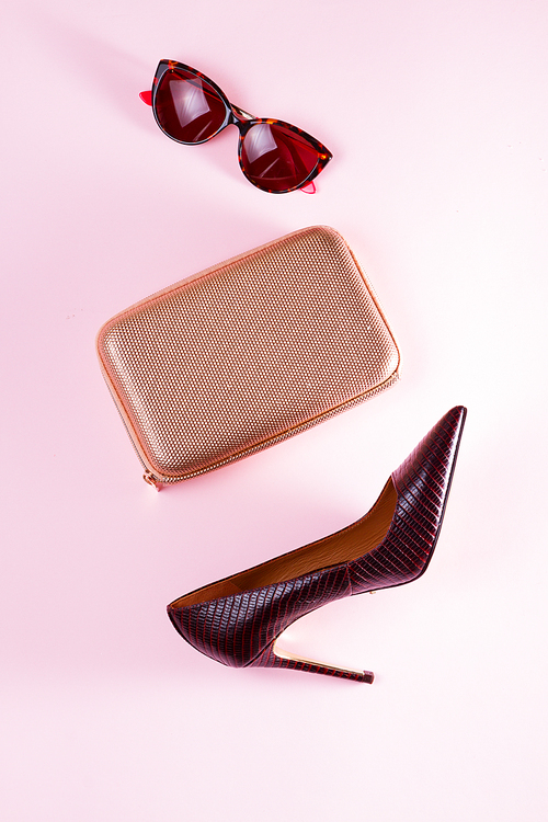 Elegant high heel shoe, golden bag and sunglasses on pink background