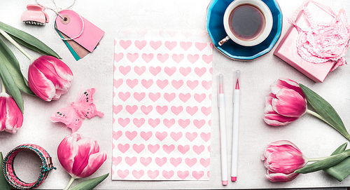 Creative pink mock up with tulips, paper package with hearts, marker pen, tags and cup of coffee on desktop, top view, frame. Layout of spring greeting card for Mothers day, Valentines day or birthday