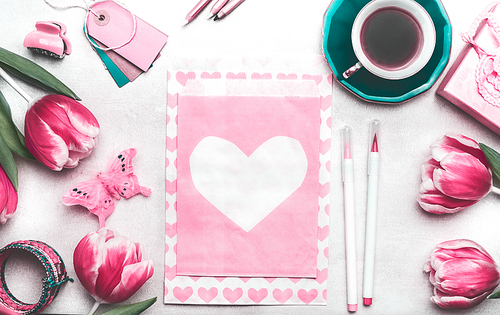 Pretty pink mock up with tulips, paper package with hearts, marker pen, tags and cup of coffee on creative desktop, top view, frame. Layout of spring greeting card for Mothers or Valentines day