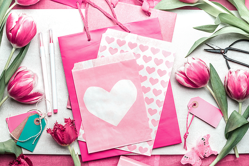 Lovely pink mock up with tulips, paper package with hearts, marker pen, tags and scissors on creative desktop, top view, frame. Layout of spring greeting card for Mothers, Valentines day or birthday