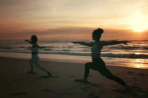 Sporty young women doing yoga practice at the beach - concept of healthy life and natural balance between body and mental development