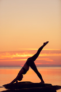 caucasian fitness woman practicing yoga on the beach at sunset