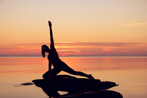 caucasian fitness woman practicing yoga on the beach at sunset