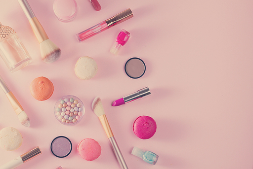 Make up products and macaroons border on pink background, retro toned