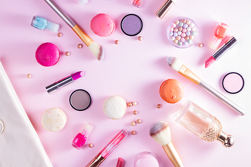 Make up products and macaroons on pink background flat lay scene