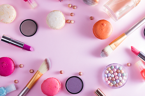 Make up products and macaroons frame on pink background