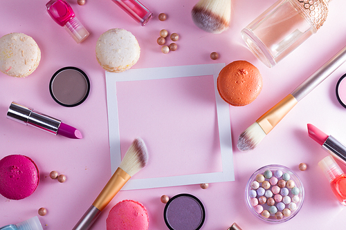 Make up products and macaroons frame with copy space on pink background