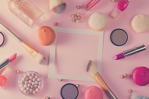 Make up products and macaroons frame with copy space on pink background, retro toned