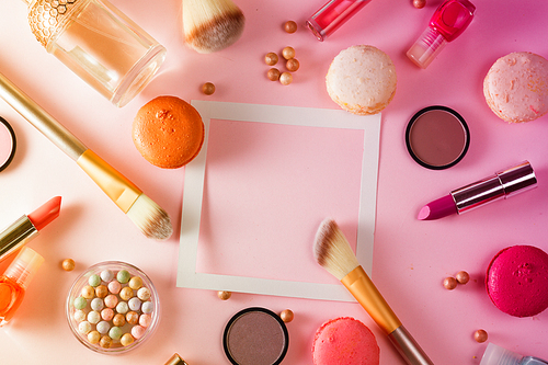 Make up products and macaroons frame with copy space on pink background, toned