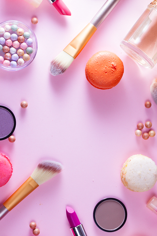 Make up products and macaroons close up flat lay scene on pink background