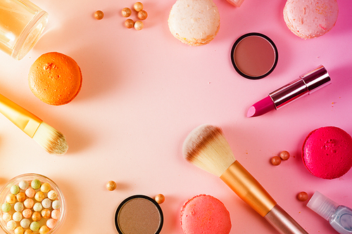 Make up products and macaroons flat lay scene on pink background, toned