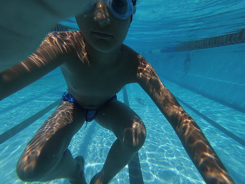 Boy in goggles swimming underwater near pools bottom and make selfie