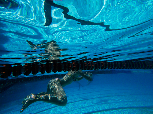 Unrecognizable girl swim underwater in pool along one of the lanes