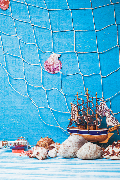 Beautiful sea composition with toy sailboat, seashell, glass bottle and fishing net on blue background