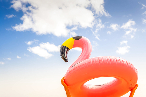 Hands holding pink inflatable flamingo head on summer sky background, retro toned
