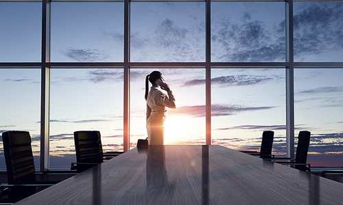 Businesswoman in night office against panoramic window in light of sunset