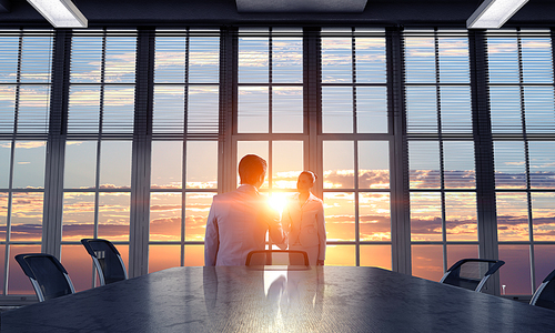 Two business people shaking hands in office in lights of sunset