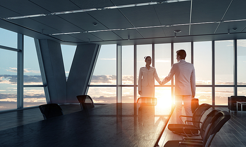 Two business people shaking hands in office in lights of sunset