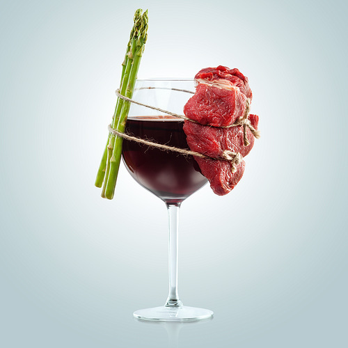 Creative concept food photo of glass of wine meat and asparagus tied with the rope on blue background.