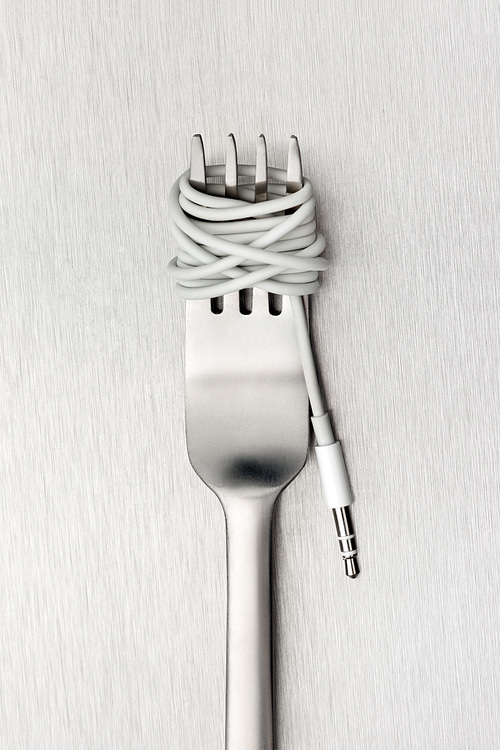 A shining fork with noodle made of cable with music jack plug in metal background.