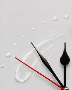 Creative concept photo of clock hands and cream on gray background.