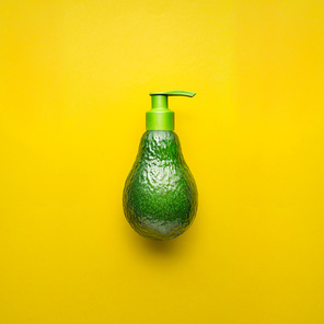 Creative concept photo of avocado with cream dispenser on yellow background.