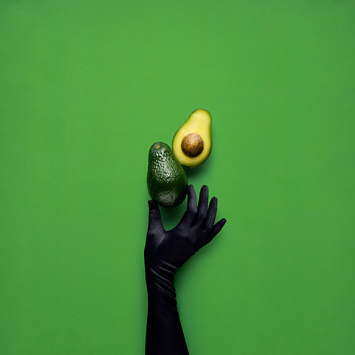 Creative concept photo of avocados with hand on green background.