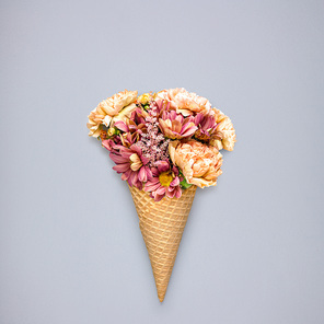 Creative still life of an ice cream waffle cone with flowers on grey background.