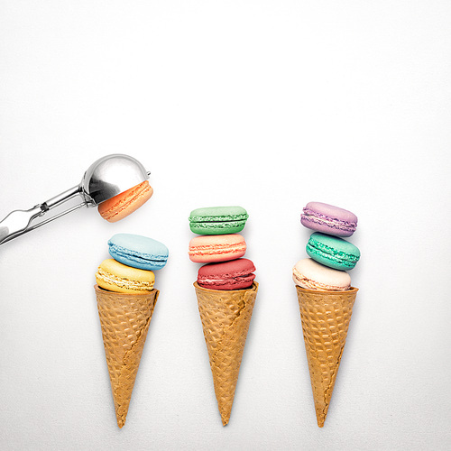Creative still life photo of three waffle cones with macaroons and spoon on grey background.