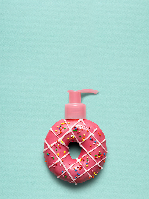 Creative still life of a tasty sweet donut with a cosmetic pump dispenser on blue background.