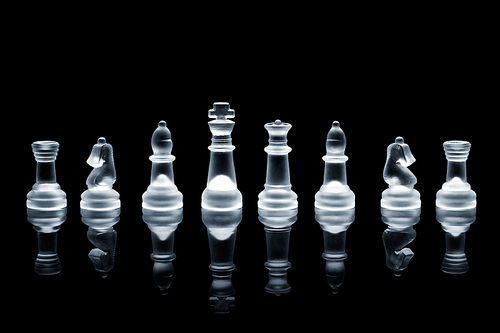 A set of semi transparent chess pieces on reflective surface.