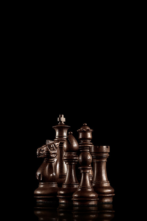 Strategy and leadership concept; black wooden chess figures standing together as a family ready for game against dark background.