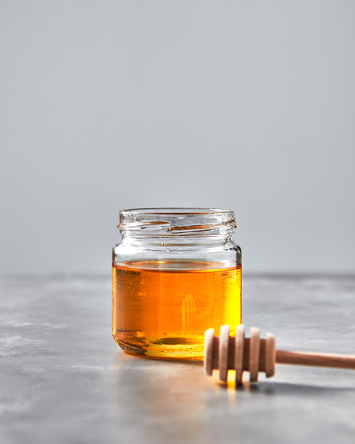 Natural sweet dessert - organic honey in a glass pot with dipper on a gray stone table, copy space. Rosh hashanah jewish concept. Traditional pure natural sweet goodness.